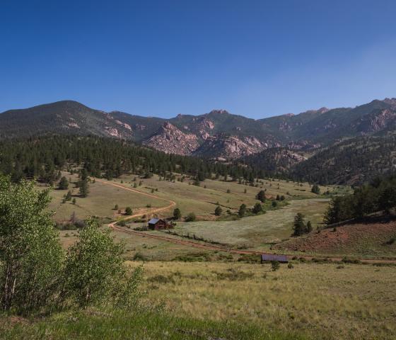 Historic ranch building sit in a meadow with rocky mountains in the background.